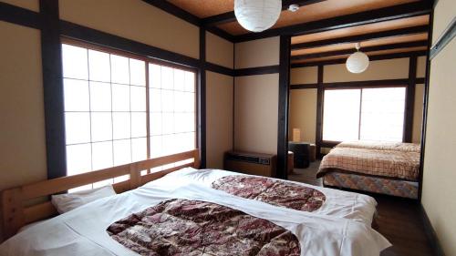 a bedroom with two beds and two large windows at Matsunokitei Irori in Otari