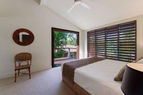 ein Schlafzimmer mit einem Bett, einem Stuhl und einem Fenster in der Unterkunft Leilani Melia - stylish 3 bedroom villa on Four Mile Beach in Port Douglas