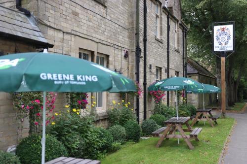 two picnic tables with umbrellas in front of a building at The Tollemache Arms in Buckminster