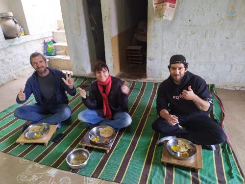 Tre uomini seduti sul pavimento con piatti di cibo di Osian Dhana Ram Ki Dhani Home Stay Osian a Osiān