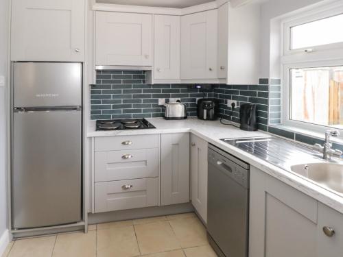 eine Küche mit weißen Schränken und einem Edelstahlkühlschrank in der Unterkunft Cherry Tree Cottage in Ballintober