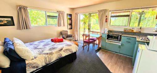 a bedroom with a bed and a kitchen with windows at Waterwheel Cottage in Upper Moutere