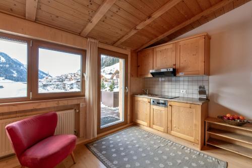 une cuisine avec une chaise rouge et quelques fenêtres dans l'établissement Apartments Heritage House Margherita, à Santa Cristina Valgardena