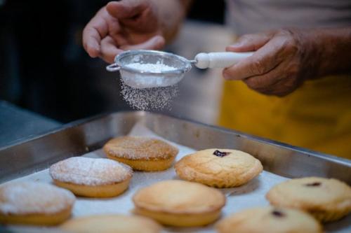 a person sprinkling powdered sugar on a tray of donuts at Hotel Scoglio Degli Achei in Torre Santa Sabina