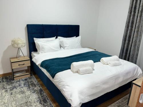 a bed with a blue headboard and two towels at Apartmani Profesional Pajkovic in Valjevo