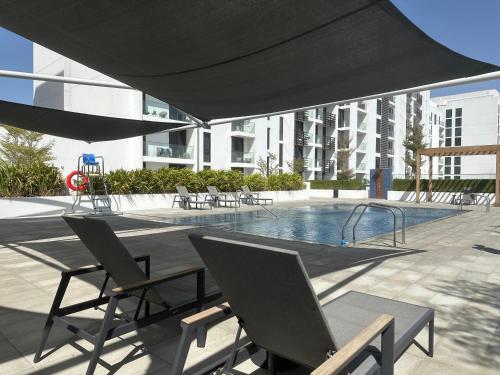 un patio con sillas y una piscina con sombrilla negra. en Modern Sanctuary W/ Pool & Gym access en Sharjah