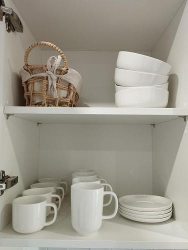 a shelf with white cups and plates and a basket at Au coucher du lac in Publier