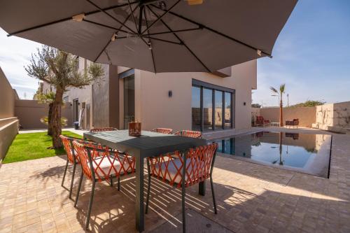 einen Tisch und Stühle mit Sonnenschirmen neben einem Pool in der Unterkunft Villa Saadia in Douar Bellouk