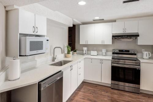 a white kitchen with a sink and a microwave at Cozy 2BR Walkout Suite Near YYC Free Parking in Calgary