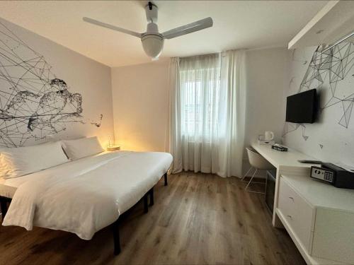 a white bedroom with a bed and a desk and a ceiling fan at Garni Hotello Sport And Relax in Riva del Garda