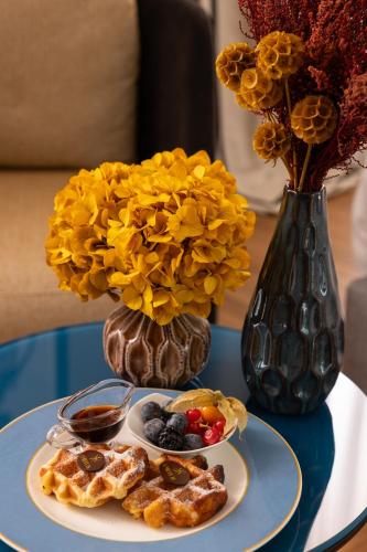 a table with a plate of waffles and a vase with flowers at Umiltà 36 in Rome