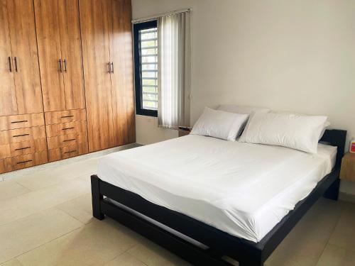 a bedroom with a bed with white sheets and wooden cabinets at Villa Nicolás Casa Campestre in Curití