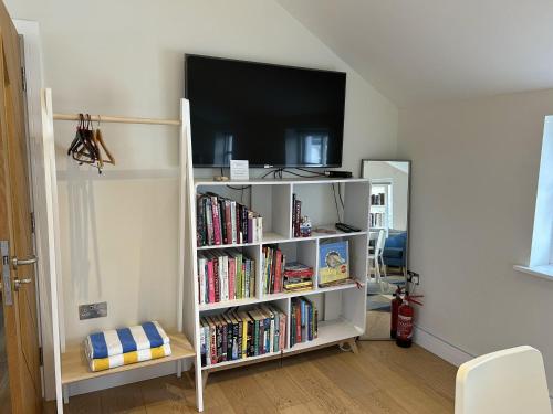 a white book shelf with books and a flat screen tv at Immaculate Studio Apartment just outside Penzance in Penzance