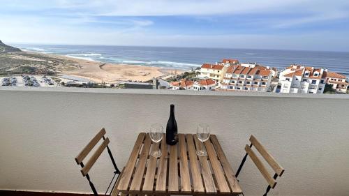 una mesa con copas de vino y una botella en el balcón en Appartement avec vue imprenable sur l'océan, en Praia da Areia Branca