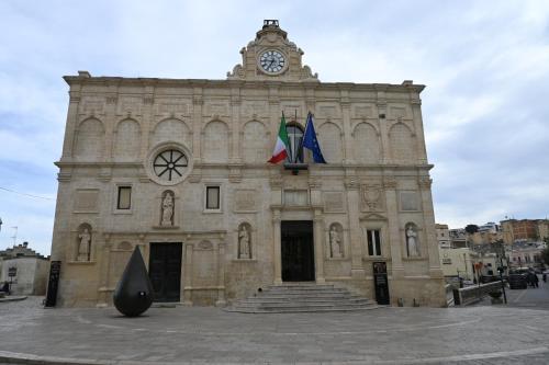 a large stone building with a clock tower and two flags at Profumi di Primavera Luxury Rooms & Suite in Matera
