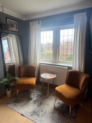 ein Wohnzimmer mit 2 Stühlen, einem Tisch und Fenstern in der Unterkunft Boutique Shrewsbury Rooms in Shrewsbury