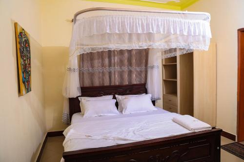 una camera con letto a baldacchino con lenzuola e cuscini bianchi di Crown Inn Bulindo a Wakiso