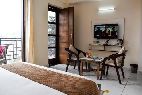 une chambre avec un lit, une table et une télévision dans l'établissement The Ivory Pine, à Shimla