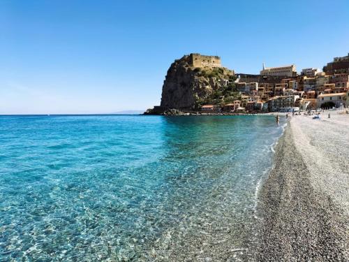 una playa de agua azul y un castillo en el fondo en B&B Omnia Scilla en Scilla