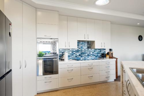 a white kitchen with white cabinets and a window at RidgeRaj - Kerikeri Holiday Home in Kerikeri
