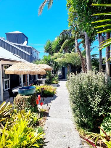 a sidewalk with a straw umbrella and chairs and plants at Southpacific Motel in Whangamata