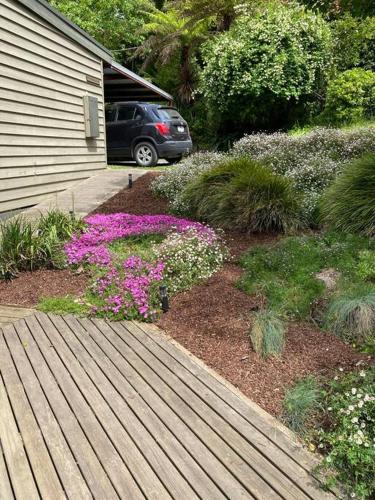 a garden with flowers and a wooden walkway next to a house at Cockatoo Rainforest Escape in Cockatoo