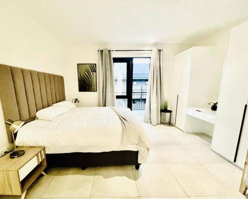 a white bedroom with a bed and a balcony at Hyde Park Sandton Luxury 2BR Top Floor in Johannesburg