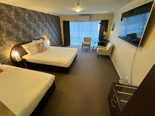 a hotel room with two beds and a chair at B-Ks Premier Motel Palmerston North in Palmerston North