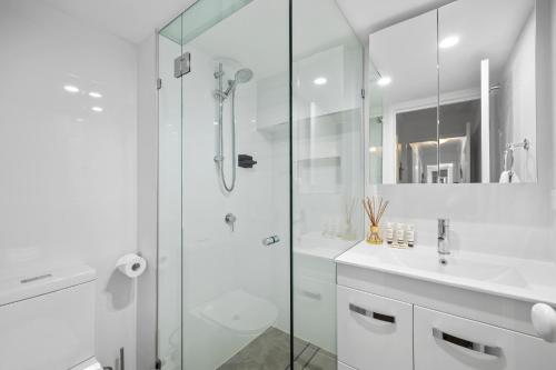 a white bathroom with a shower and a sink at Beachside 3-Bed with Pool, BBQ, Gym & Tennis Court in Marcoola