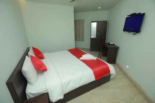 a bedroom with a bed with red pillows and a television at Premier Tourist Home in Kunnamkulam