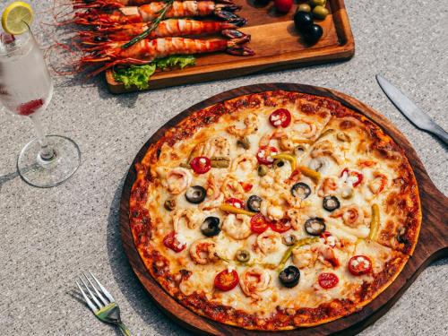a pizza on a table with a glass of wine at De Garland Palolem - AM Hotel Kollection in Palolem