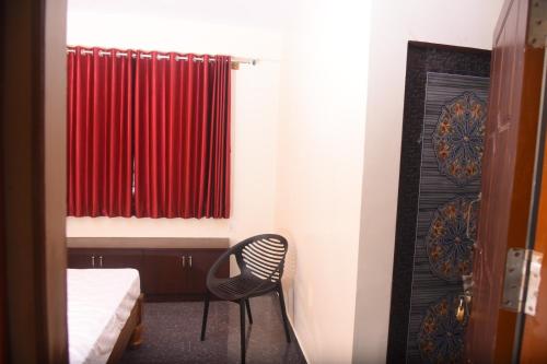 シモガにあるShiva Deluxe Lodgeのベッド1台、椅子、赤いカーテンが備わる客室です。