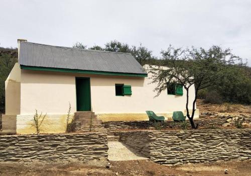 a house with two green chairs in front of it at Adam se Huisie - become a part of history... in Calitzdorp