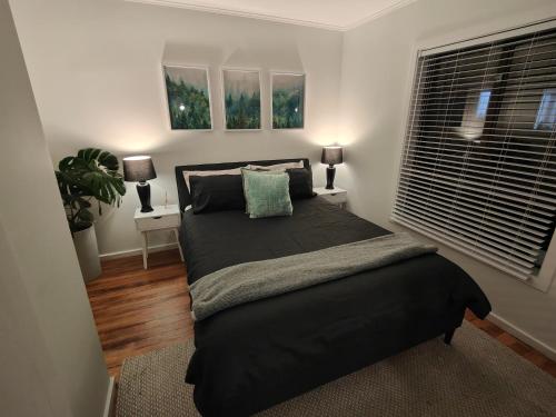 a bedroom with a black bed and two windows at Beautiful haven near airport! in Christchurch