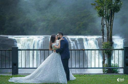 a bride and groom kissing in front of a waterfall at Rainforest Resort in Athirappilly