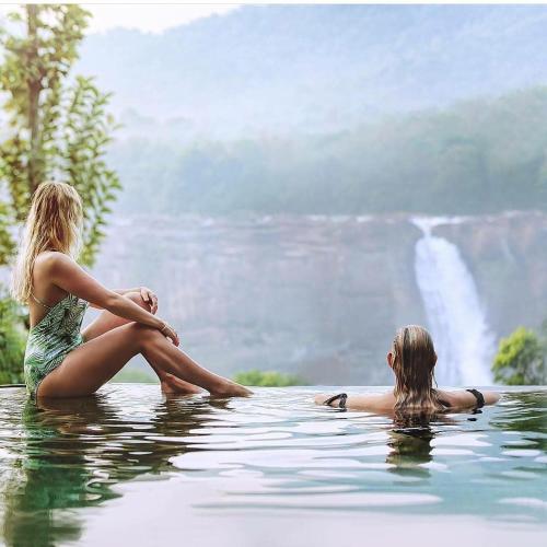 two women sitting in the water in front of a waterfall at Rainforest Resort in Athirappilly