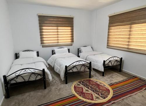 two beds in a room with two windows and a rug at Eman house in Wadi Musa