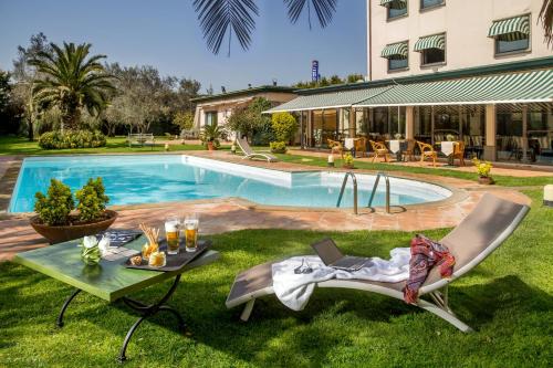 una piscina con 2 sillas y una mesa en el césped en Best Western Park Hotel Roma Nord, en Fiano Romano