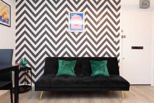 um sofá preto com duas almofadas verdes numa sala de estar em Modern flat - Sleeps 3 - London em Enfield