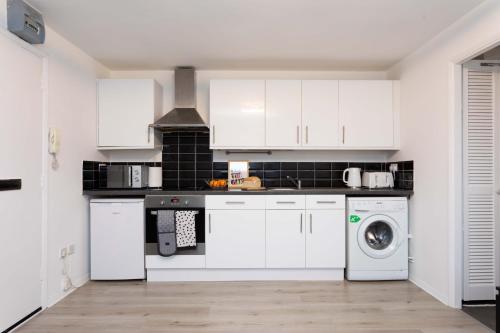 a kitchen with white cabinets and a washer and dryer at Modern flat - Sleeps 3 - London in Enfield