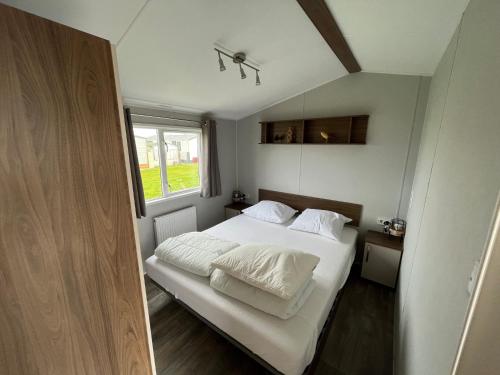 1 dormitorio con 1 cama con sábanas blancas y ventana en Neues Ferienhaus Chalet Nr73 direkt am Wattenmeer, komplett eingezäunt, en Westerland