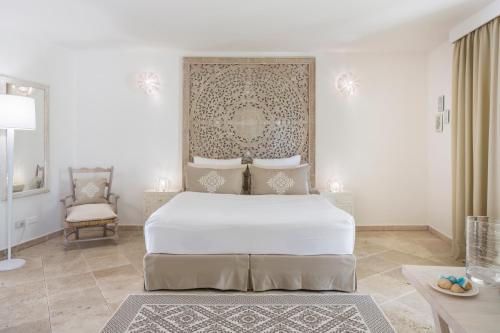 a white bedroom with a bed and a chair at Falkensteiner Resort Capo Boi in Villasimius