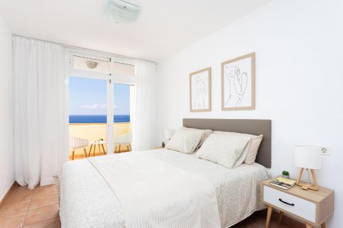 a white bedroom with a bed and a view of the ocean at Frontline Duplex Las Arenitas with pool in Candelaria