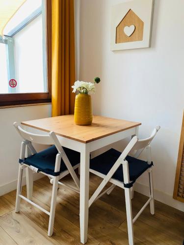 einen Tisch mit zwei Stühlen und eine gelbe Vase mit Blumen in der Unterkunft Studio au calme avec terrasse - hauteurs de Rouen in Bihorel