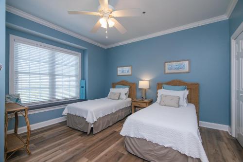 a blue bedroom with two beds and a ceiling fan at Retreat 5B - Edisto Blessing in Edisto Island