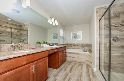 uma casa de banho com 2 lavatórios, um chuveiro e uma banheira. em 4776JW VILLA 6 BED/5 BA (SANITIZED) em Kissimmee