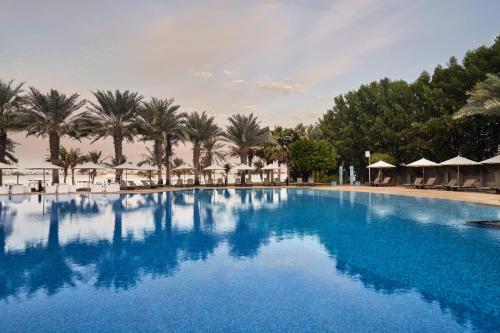 a large blue swimming pool with palm trees and umbrellas at Rixos The Palm Hotel & Suites - Ultra All Inclusive in Dubai