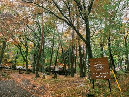a sign in the middle of a forest with trees at Nagano GLAMPINGBASE enCamp in Shiojiri