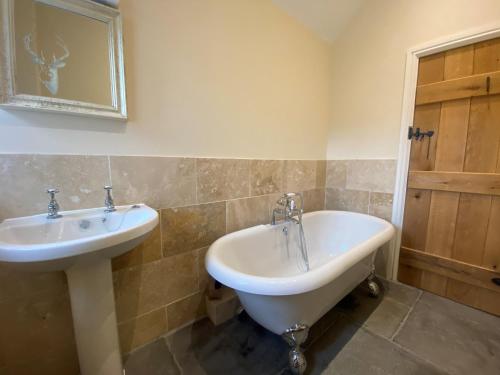 ein Badezimmer mit einem Waschbecken und einer Badewanne neben einem Spiegel in der Unterkunft The Udderhouse - Udderly Unforgettable Retreat in Donyatt