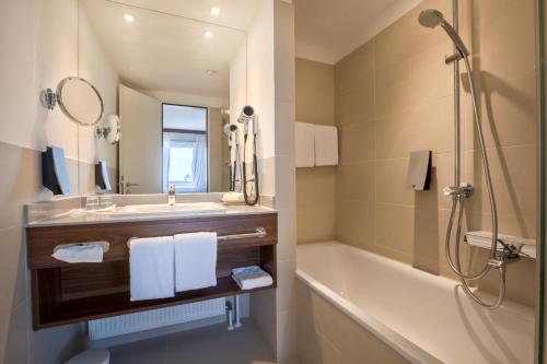 a bathroom with a sink and a tub and a mirror at Fora Hotel Hannover by Mercure in Hannover